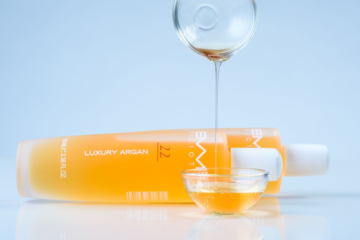 Golden Moroccan argan oil being poured from a bottle into a glass bowl