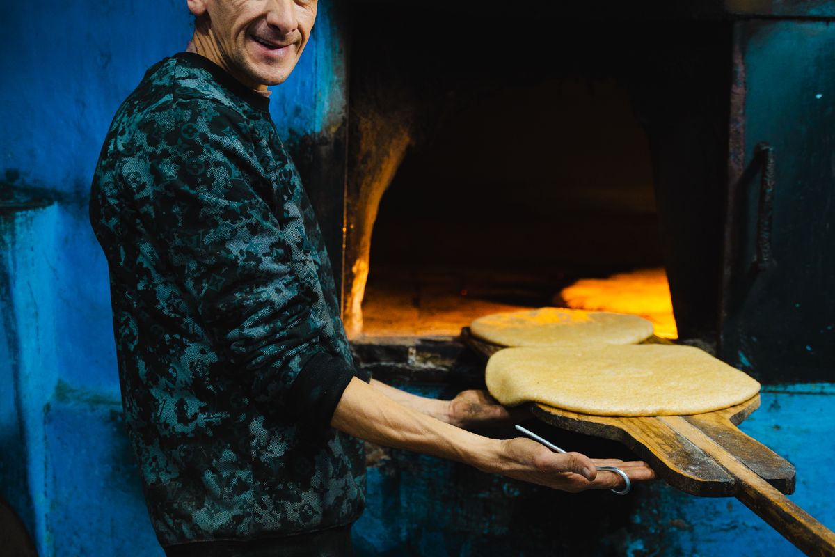 Moroccan baker preparing bread at a traditional brick oven in Chefchaouen, Morocco