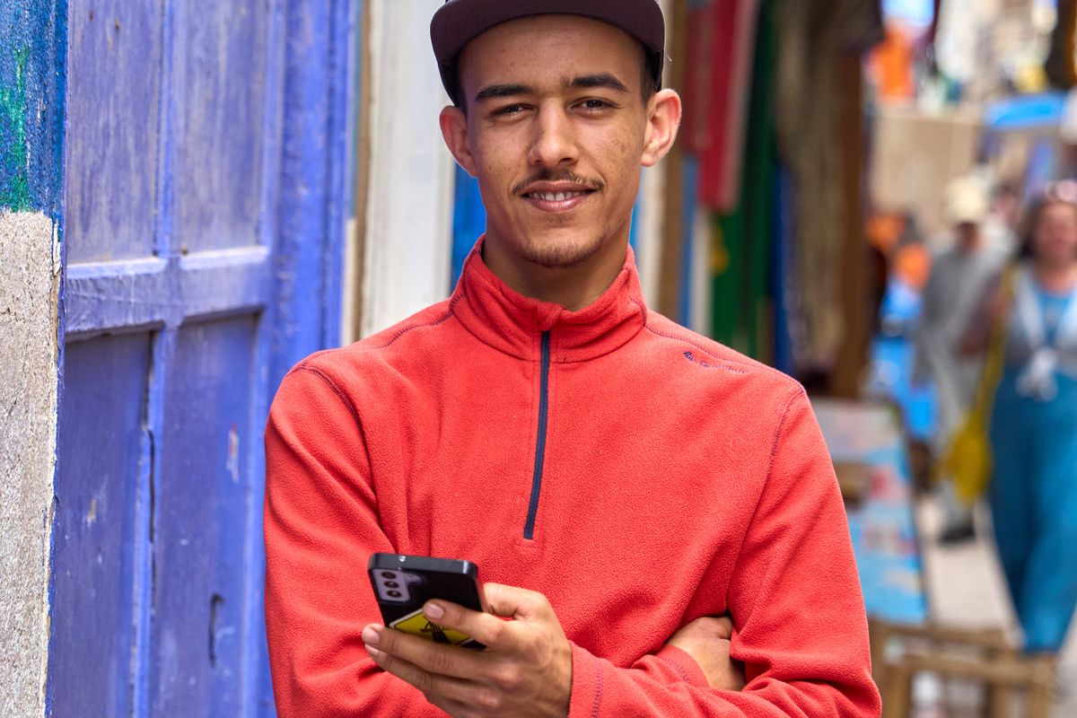 Young man holding a smartphone beside a colourful wall in Essaouira, Morocco