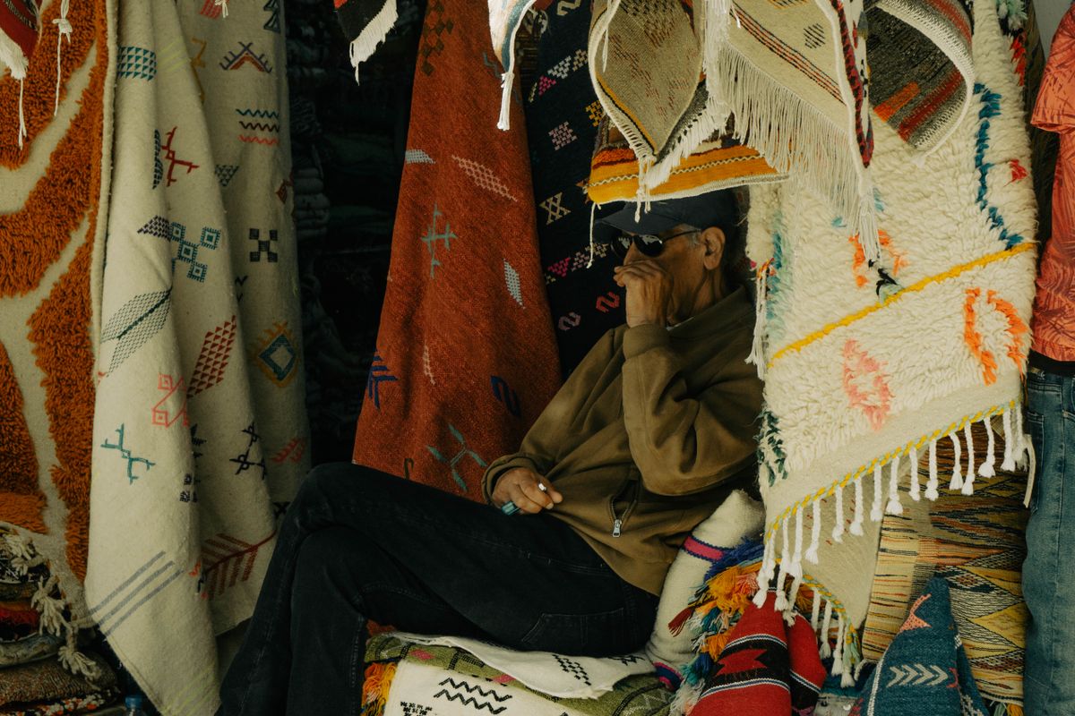 Man sitting among colourful rugs in a market stall in Essaouira, Morocco