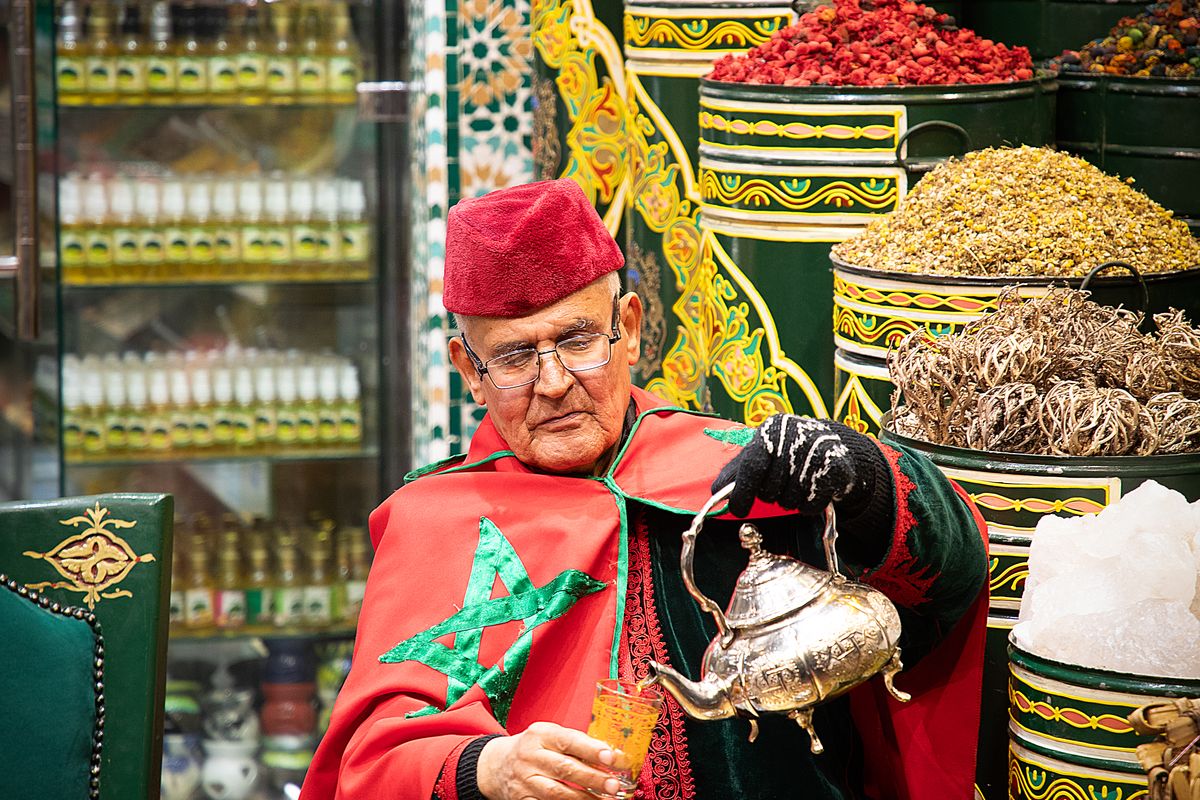 Elderly man in traditional dress pouring mint tea in a market in Marrakech, Morocco
