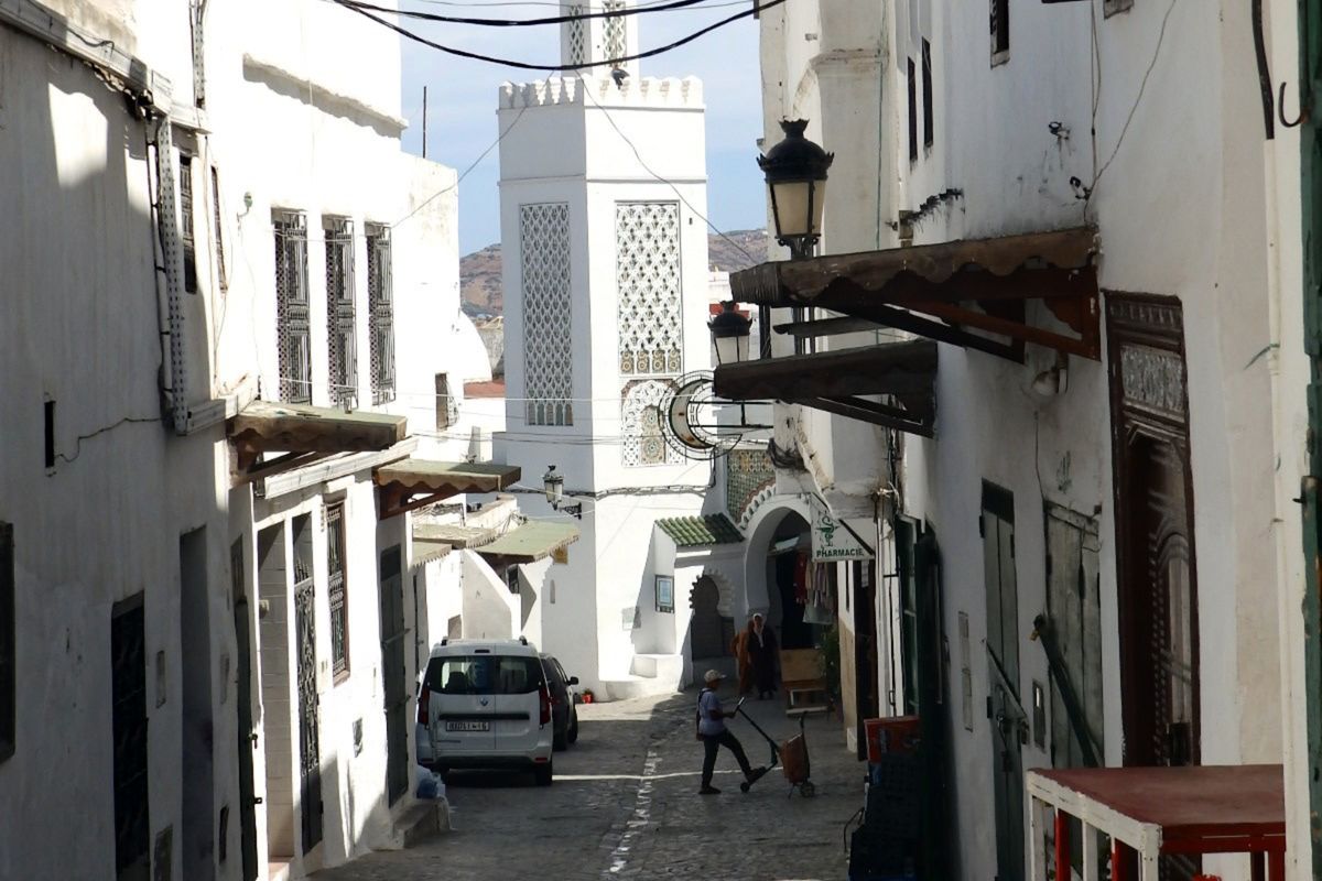 Narrow lane between white houses in the medina of Tetouan, Morocco, with a minaret in the distance