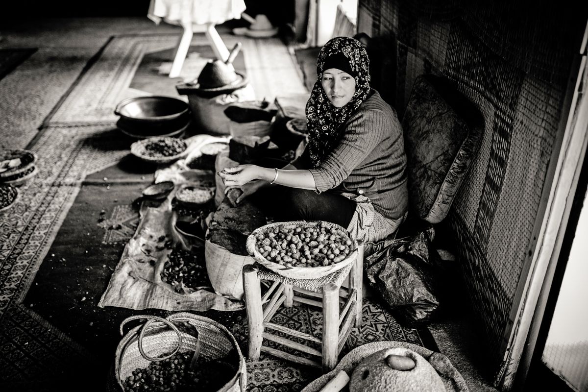 Black and white photo of a Moroccan woman cracking argan nuts by hand to make argan oil